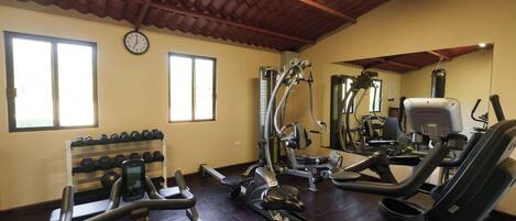 Un gimnasio con máquinas de cardio, mancuernas y un reloj en la pared.