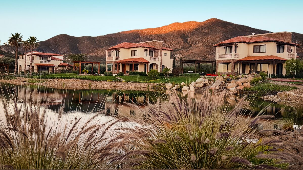 Zona residencial con tres casas, un estanque y una montaña al fondo.