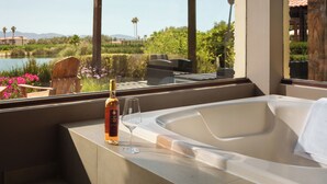 A hot tub with a bottle and glass on a balcony overlooking a garden and a body of water.