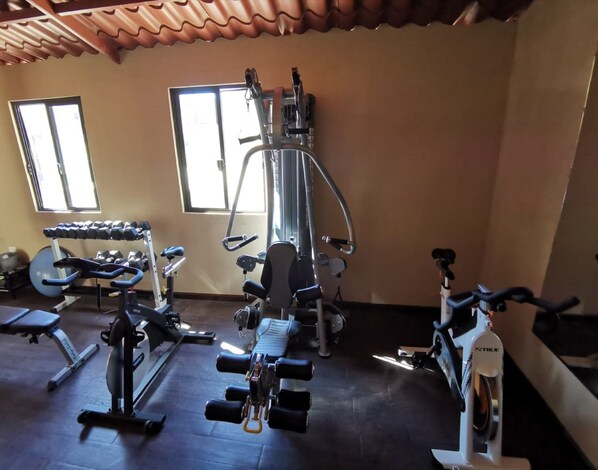 Un gimnasio con equipo de ejercicio variado, incluyendo mancuernas, una banca y una bicicleta estática.