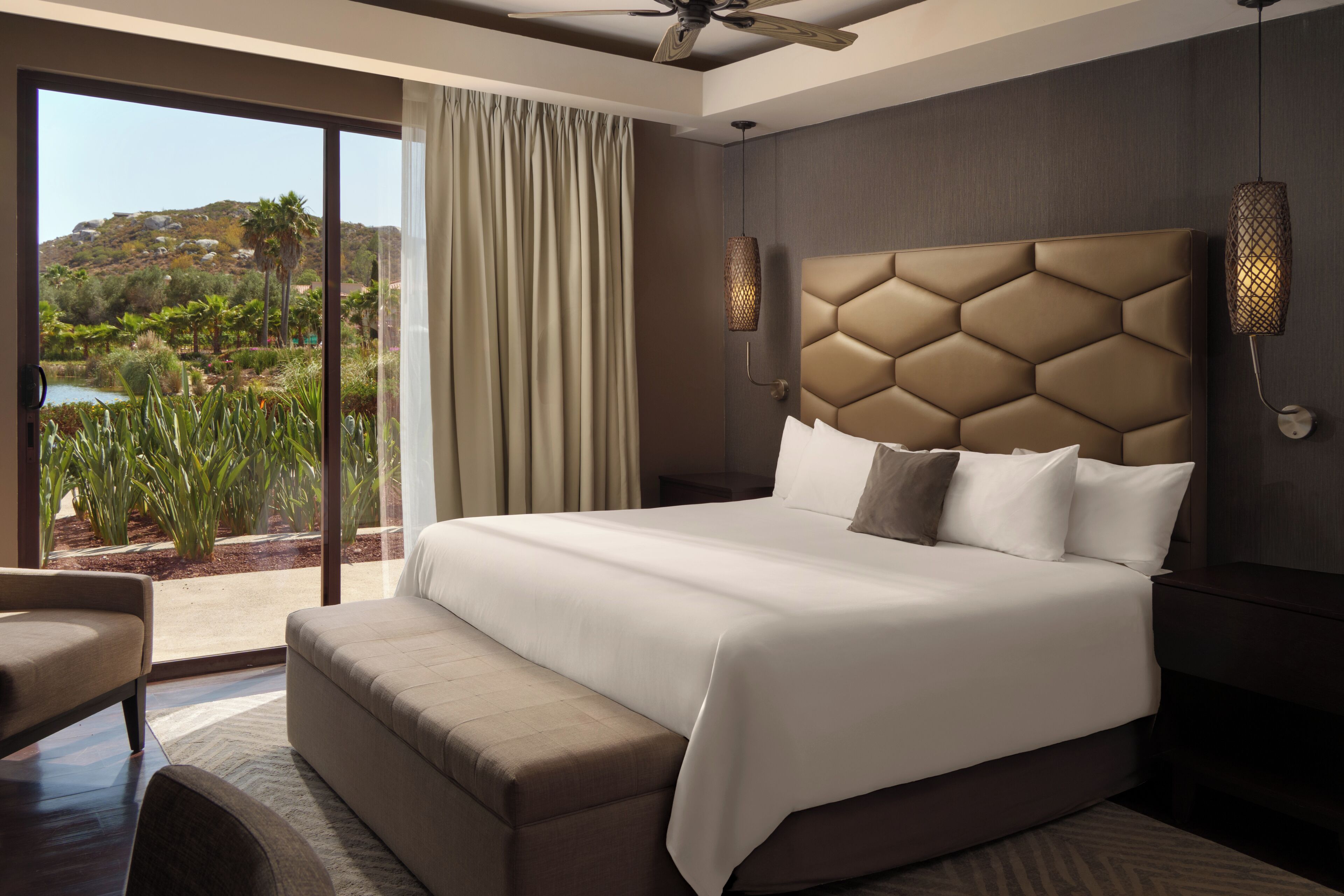 Una habitación de hotel moderna con una cama grande, vistas a un jardín ajardinado y un ventilador de techo.