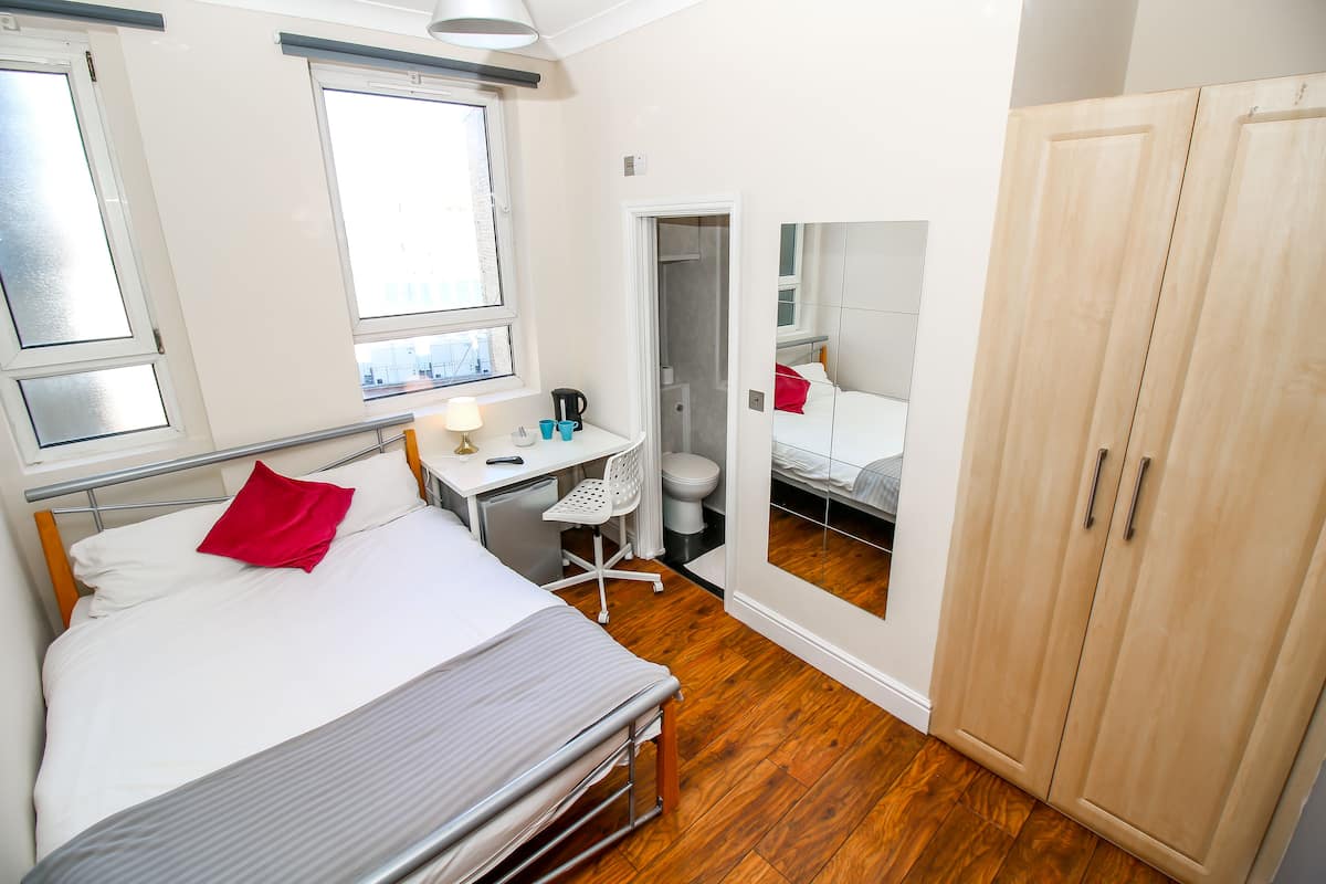 A bedroom with a bed, desk, chair, wardrobe, and a mirror.