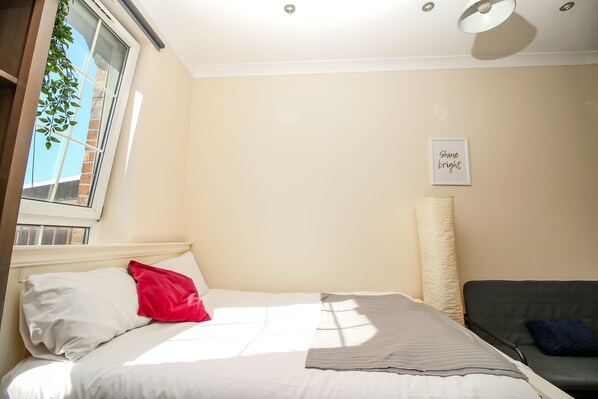 A bed with white and red pillows, a grey striped blanket, and a wall-mounted lamp. - Private Ensuite Room Liverpool Street (London)