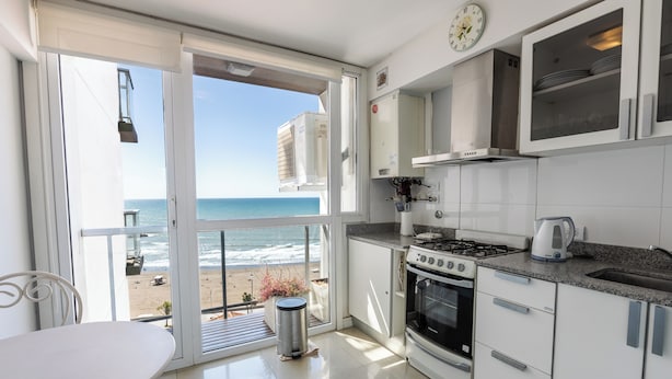 A kitchen with a view of the beach, a dining area, and a trash can. - DeptosVip (Mar del Plata)