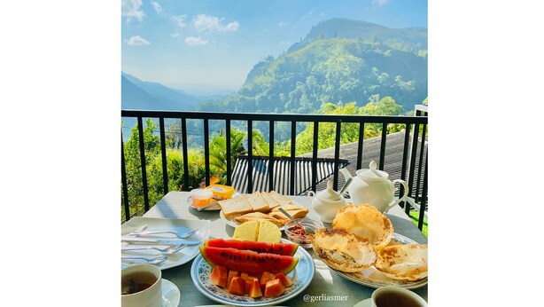 A table set with breakfast items, including toast, fruit, and a teapot, overlooking a mountainous landscape. - Paraiso Guest House (Ella)