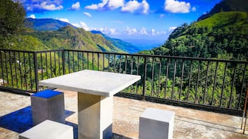 Ein Balkon mit Tisch und zwei Hocker, mit Blick auf eine gebirgige Landschaft.