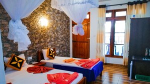 A room with two beds, a stone wall, a wooden door, and a view of the outside. - Paraiso Guest House (Ella)