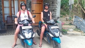 Two individuals on scooters parked in front of a stone building with a wooden door and a chair visible inside. - Paraiso Guest House (Ella)