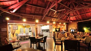 Comedor interior con mesas y sillas, una cocina al fondo, y un techo de paja.