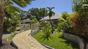 A tropical garden with a stone pathway leading to a house with a tiled roof. - Le Laugaut's Bungalows (Nosy Be)