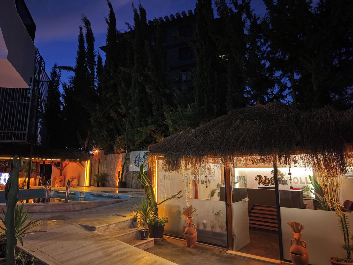A hotel reception area with a pool, surrounded by tropical plants and a thatched-roof structure.