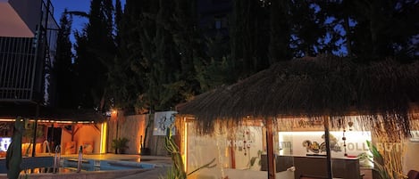 A hotel reception area with a pool, surrounded by tropical plants and a thatched-roof structure.
