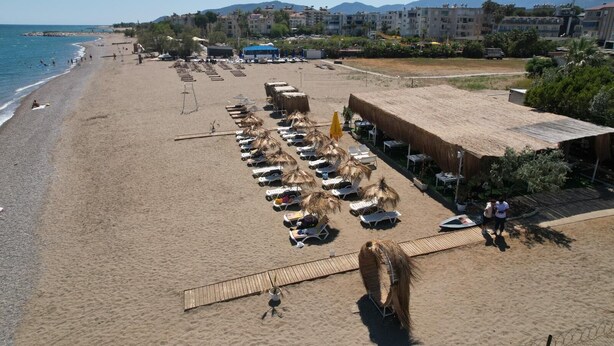 A beach with sun loungers and umbrellas, a wooden deck, and buildings in the background. -  Rolli Butik Hotel (Anamur)