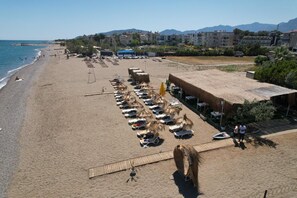 A beach with sun loungers and umbrellas, a wooden deck, and buildings in the background. -  Rolli Butik Hotel (Anamur)