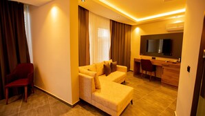 A modern living room with a sofa, a red chair, a desk, and a television. -  Rolli Butik Hotel (Anamur)