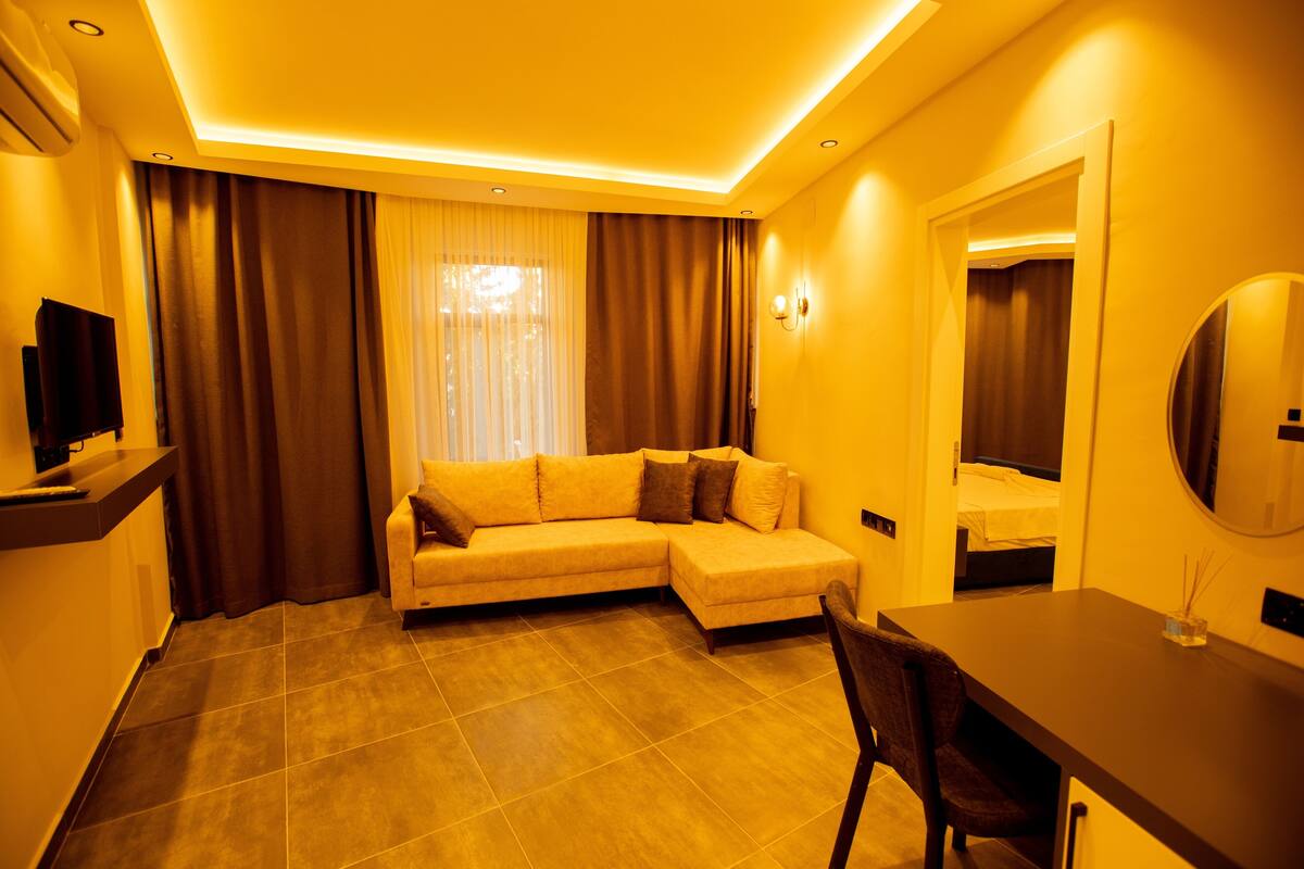 A modern hotel room with a sectional sofa, a dining table, and a TV.