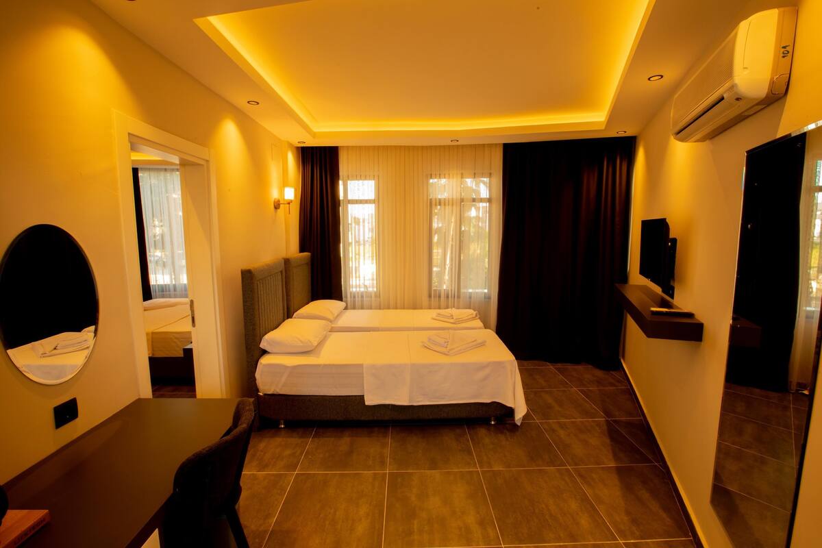 A hotel room with a bed, a desk, a chair, a mirror, and an air conditioning unit.