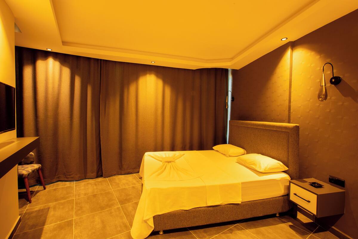 A hotel room with a bed, a nightstand, a chair, and a large window with curtains.