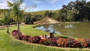 A tranquil garden with a pond, a thatched-roof gazebo, and vibrant flower beds. - Pousada e Pesca Esportiva Fazolin (Socorro)