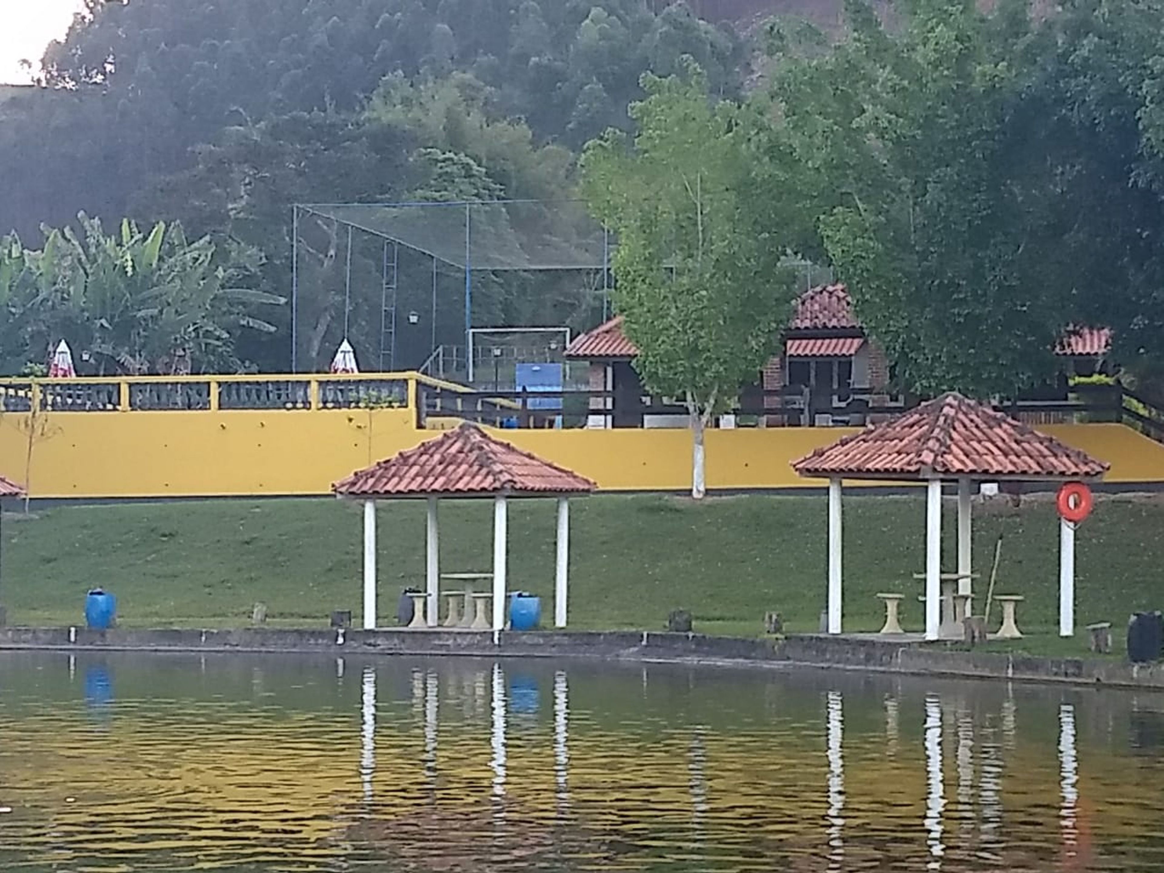 A lakeside view with a yellow building, a gazebo, and a small pavilion.