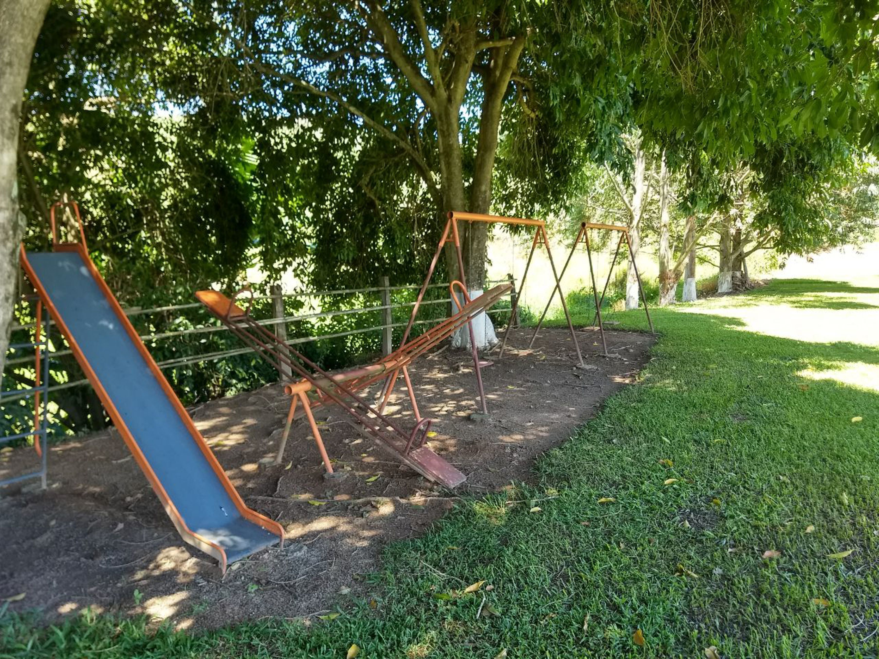 A playground with swings and a slide, surrounded by trees and grass.