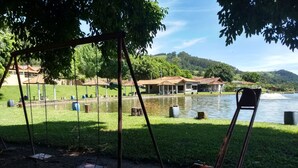 A park with swings, a pond, and buildings with red roofs in the background. - Pousada e Pesca Esportiva Fazolin (Socorro)