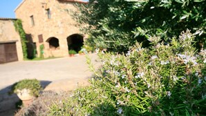 A stone building with arched doorways and a garden with white flowers in the foreground. - Can Barrull (Palau-Sator)
