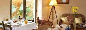 A dining area with a table set for breakfast, a wicker chair, a lamp, and a vase with yellow flowers. - Can Barrull (Palau-Sator)