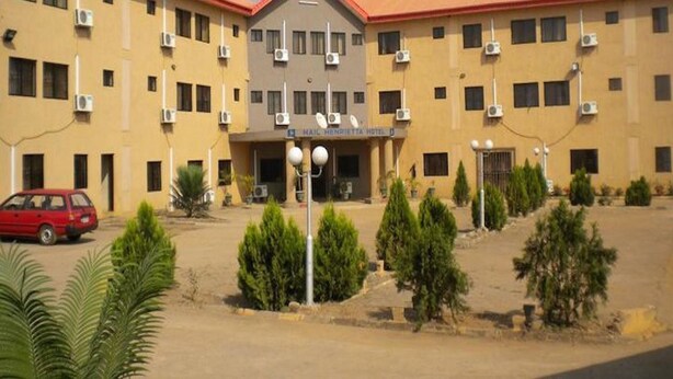 Ein Hotel mit zentralem Eingang, mehreren Klimaanlagen und einem roten Auto vor der Fassade.