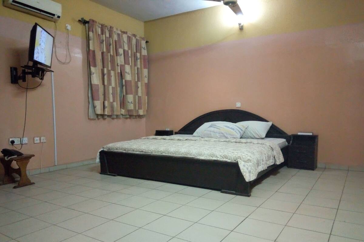 Un dormitorio con cama, mesita de noche, televisor montado en la pared y ventilador de techo.
