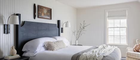 A bedroom with a bed, bedside tables, a nightstand, a window, and a wall-mounted lamp.