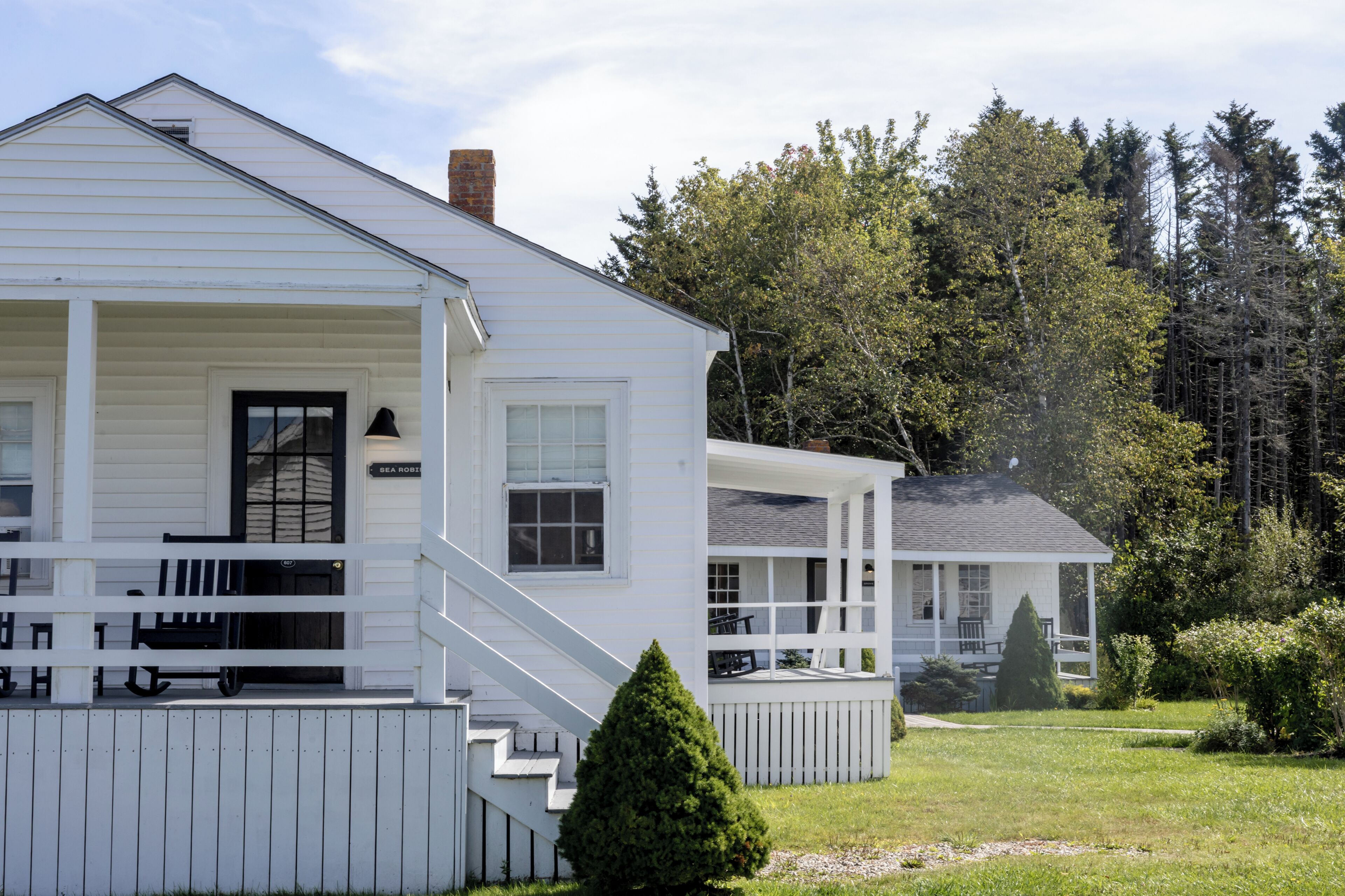 A white two-story house with a porch, a chimney, and a small garden.