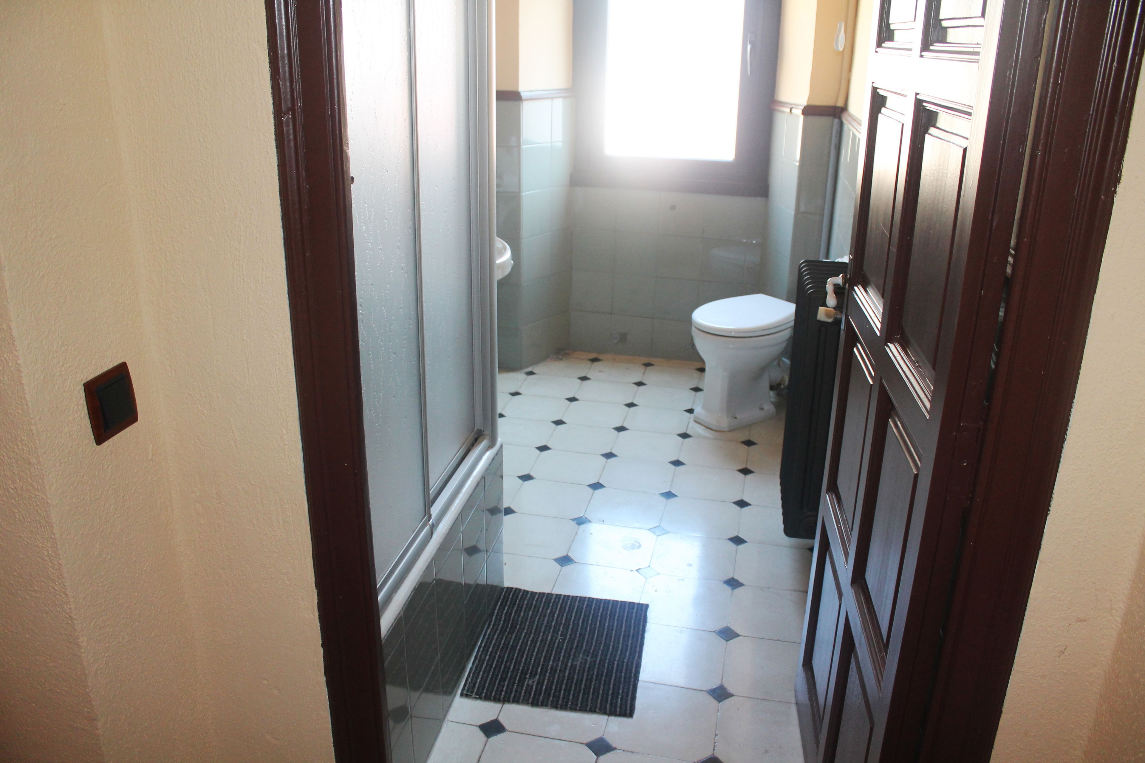Un baño con inodoro, ducha y suelo de baldosas.