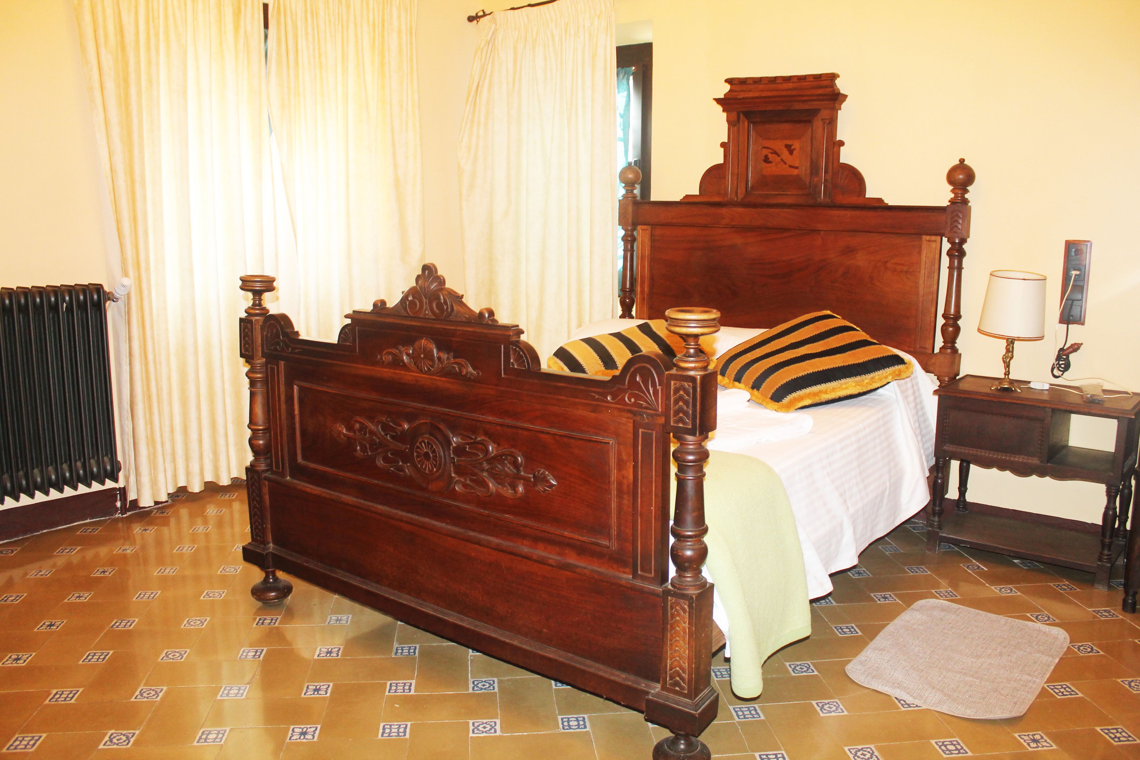 A traditional wooden bed with a headboard, a bedside table with a lamp, and a patterned floor.