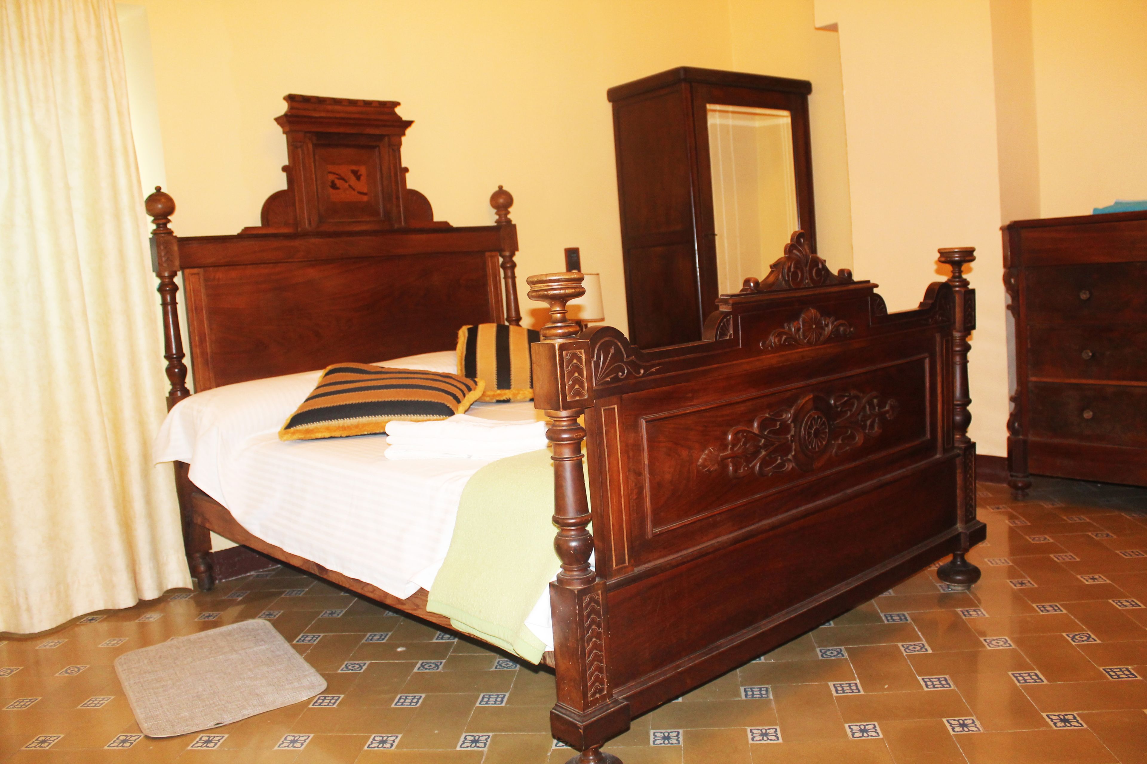 Una cama con dosel de madera con un espejo encima, una mesita de noche y un suelo estampado.
