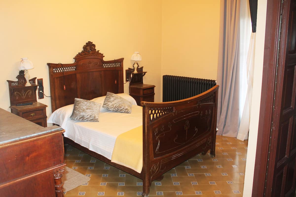 A traditional wooden bed with a headboard, two bedside tables with lamps, a radiator, and patterned floor tiles.