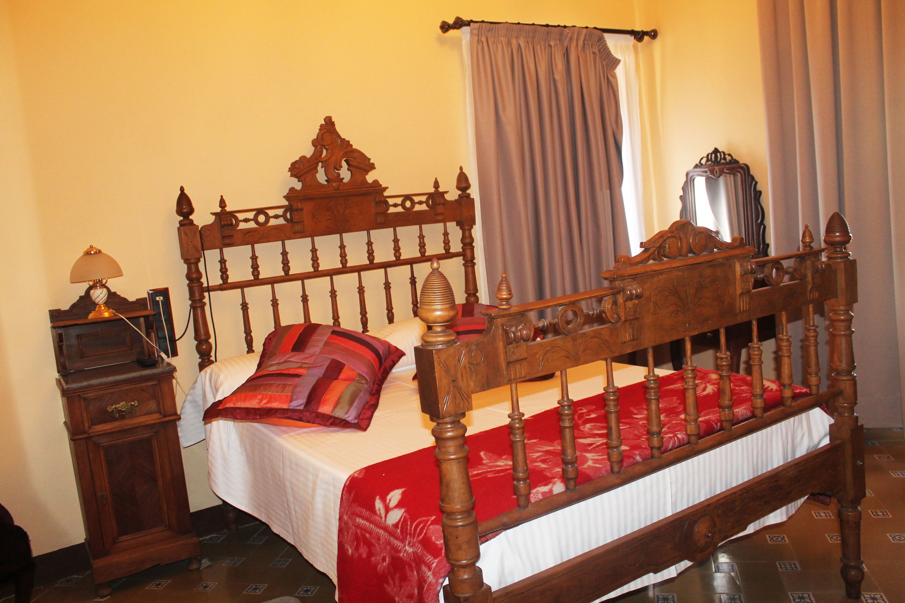 Una cama de madera con cabecera, una mesita de noche con lámpara y una colcha roja.