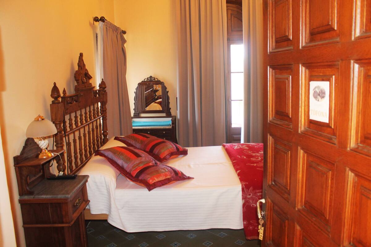 A hotel room with a wooden bed, a nightstand with a lamp, a mirror, and a door with a sign.