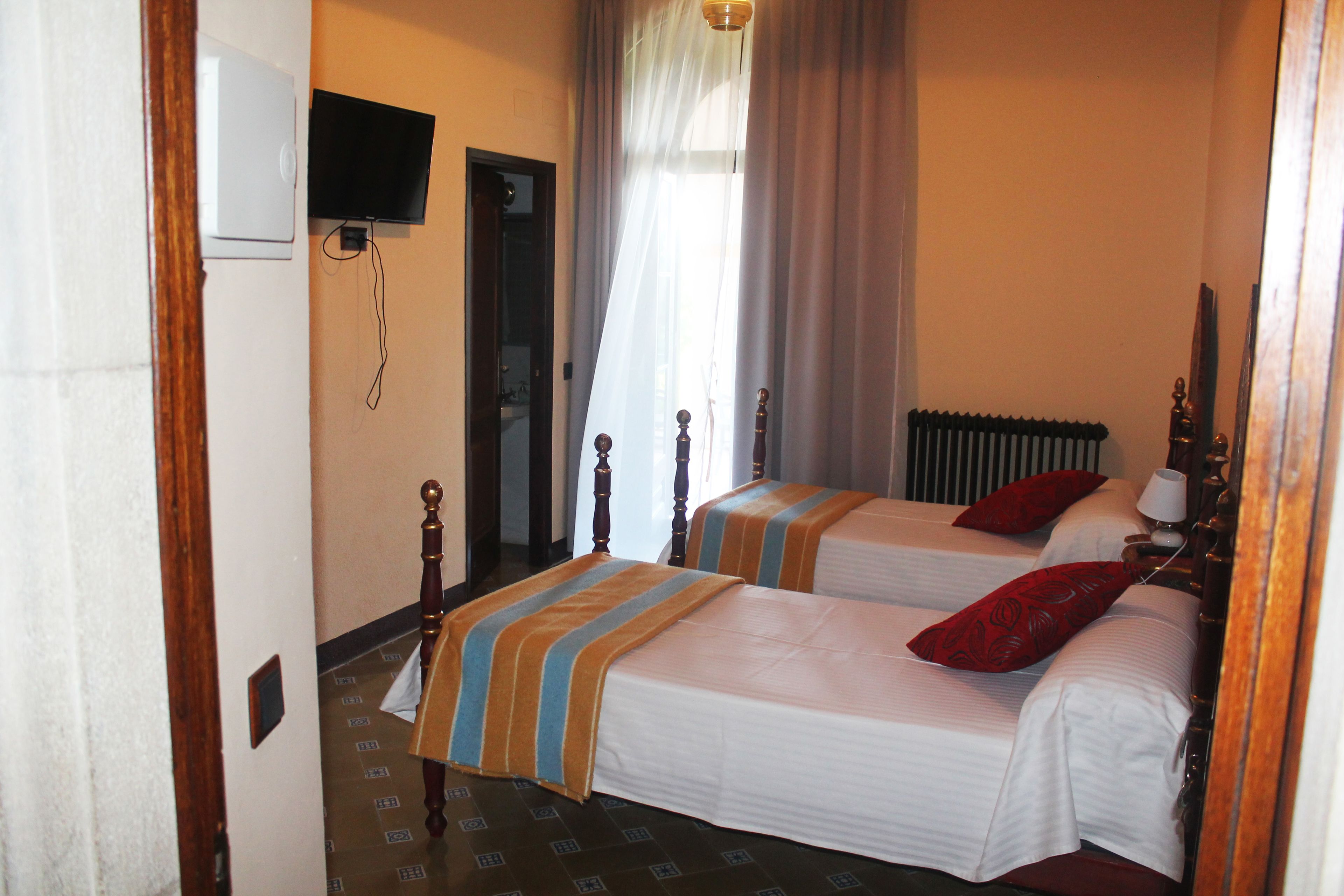 Une chambre d’hôtel avec deux lits, un téléviseur fixé au mur, un radiateur et une fenêtre avec des rideaux.