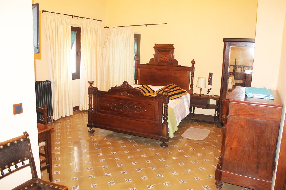 A room with a wooden bed, a wooden nightstand with a lamp, a wooden dresser, and a mirror.