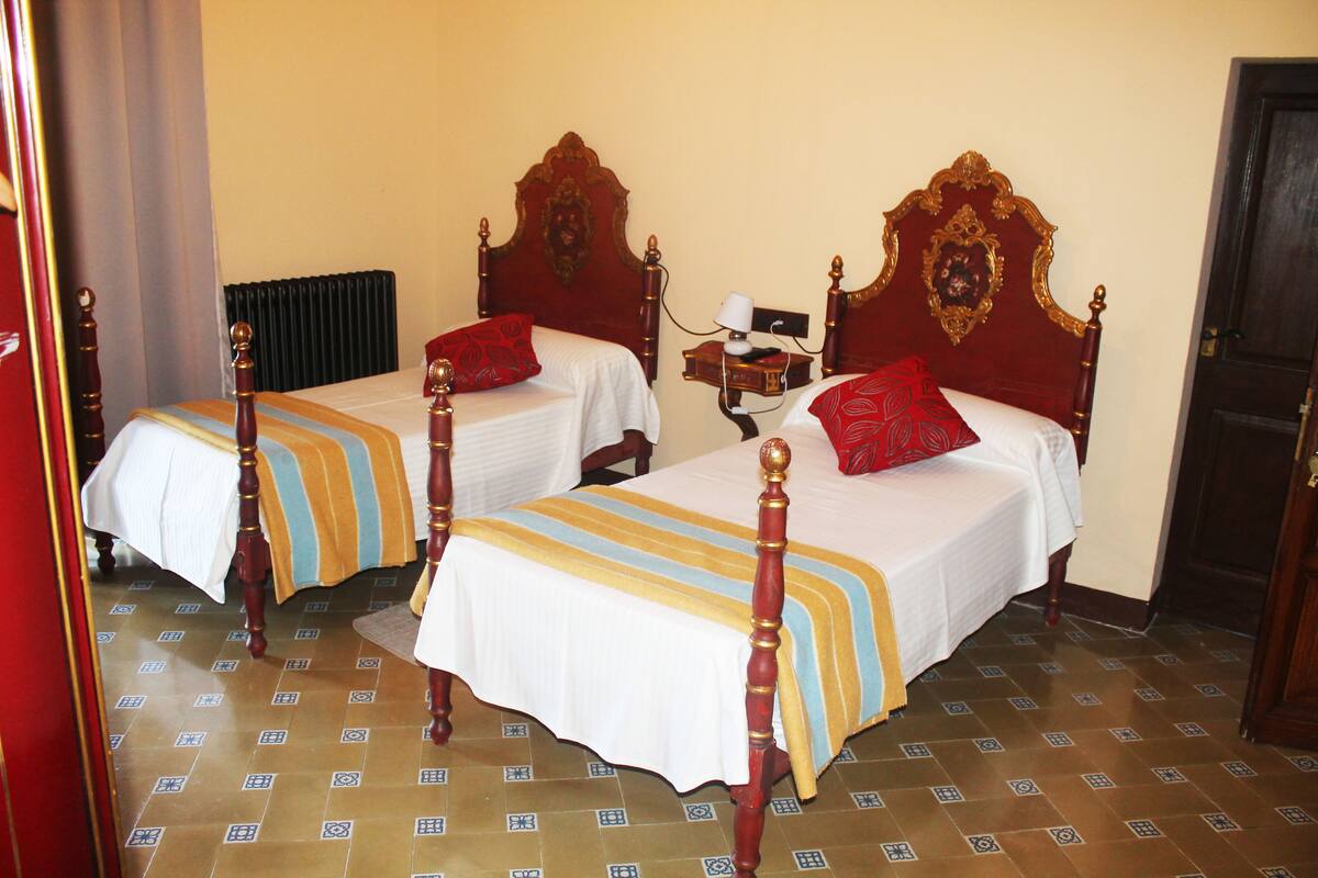 Two double beds with wooden frames and red headboards, a bedside table with a lamp, and a radiator on the wall.