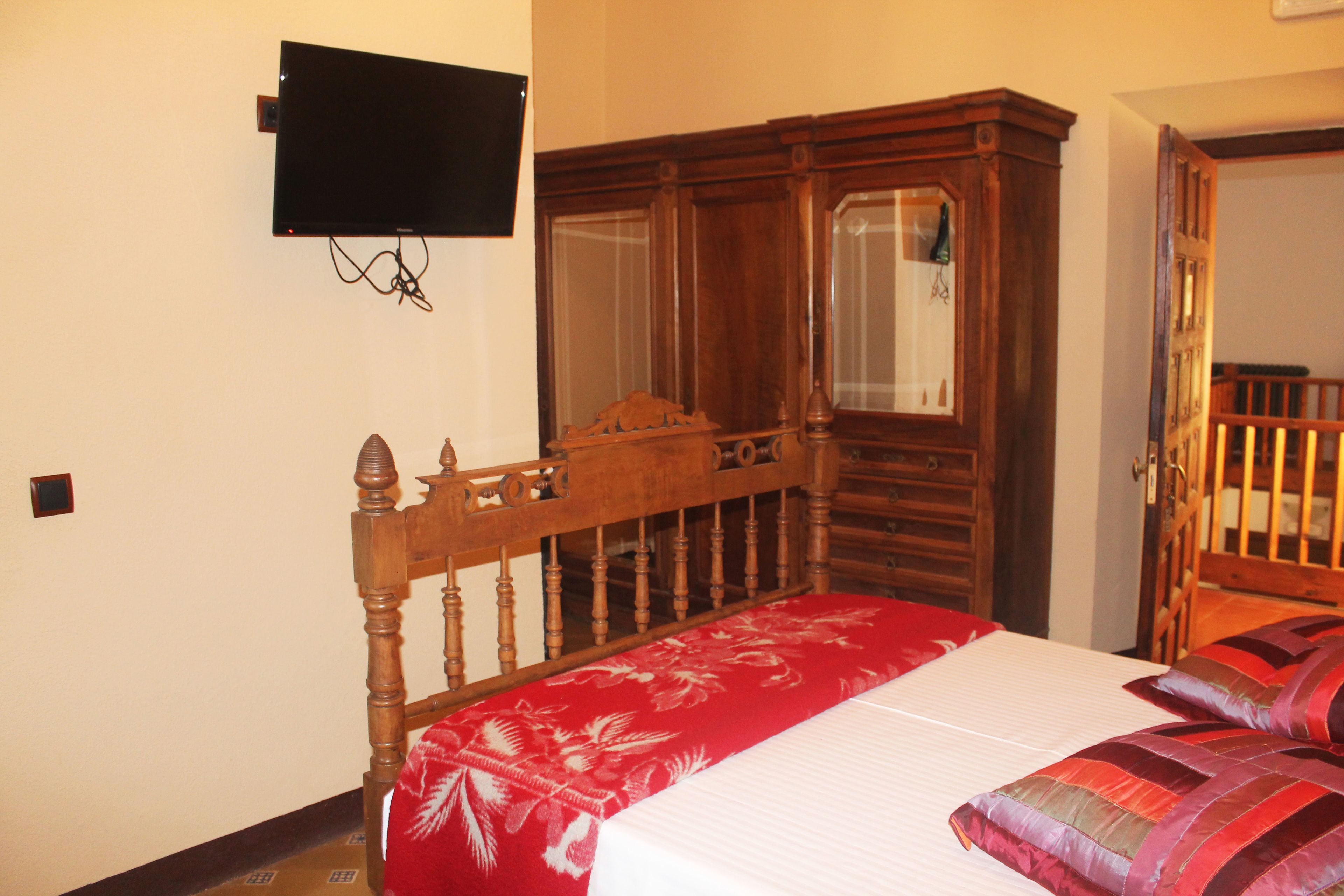 A bedroom with a wooden headboard, a flat-screen TV mounted on the wall, and a wooden wardrobe.