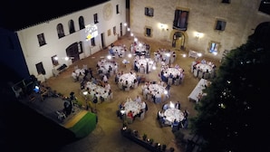 A courtyard with multiple round tables set up for dining, surrounded by a building with arched windows and a clock. - Hostal Rural Mas Blanc (Sant Marti de Centelles)