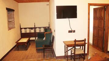 Una habitación con techo de madera, un televisor montado en la pared, una puerta de madera, un sillón verde, una mesa de madera y una silla de madera.