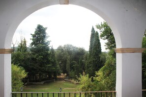 A view through an arched window of a garden with trees and a stone pathway. - Hostal Rural Mas Blanc (Sant Marti de Centelles)