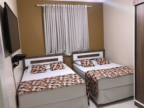A hotel room with two beds, each with patterned bedding and pillows, a television mounted on the wall, and a curtain rod above the beds. - APARTAMENTO EM COPACABANA (Rio de Janeiro)