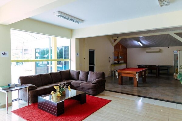 A spacious living area with a brown sofa, a red rug, a pool table, and a large window offering a view of the outside.