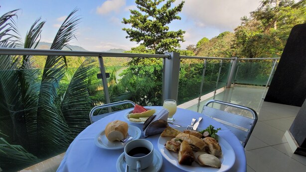 A table set with food and drinks on a balcony overlooking a lush landscape. - Carajas Hotel (Parauapebas)