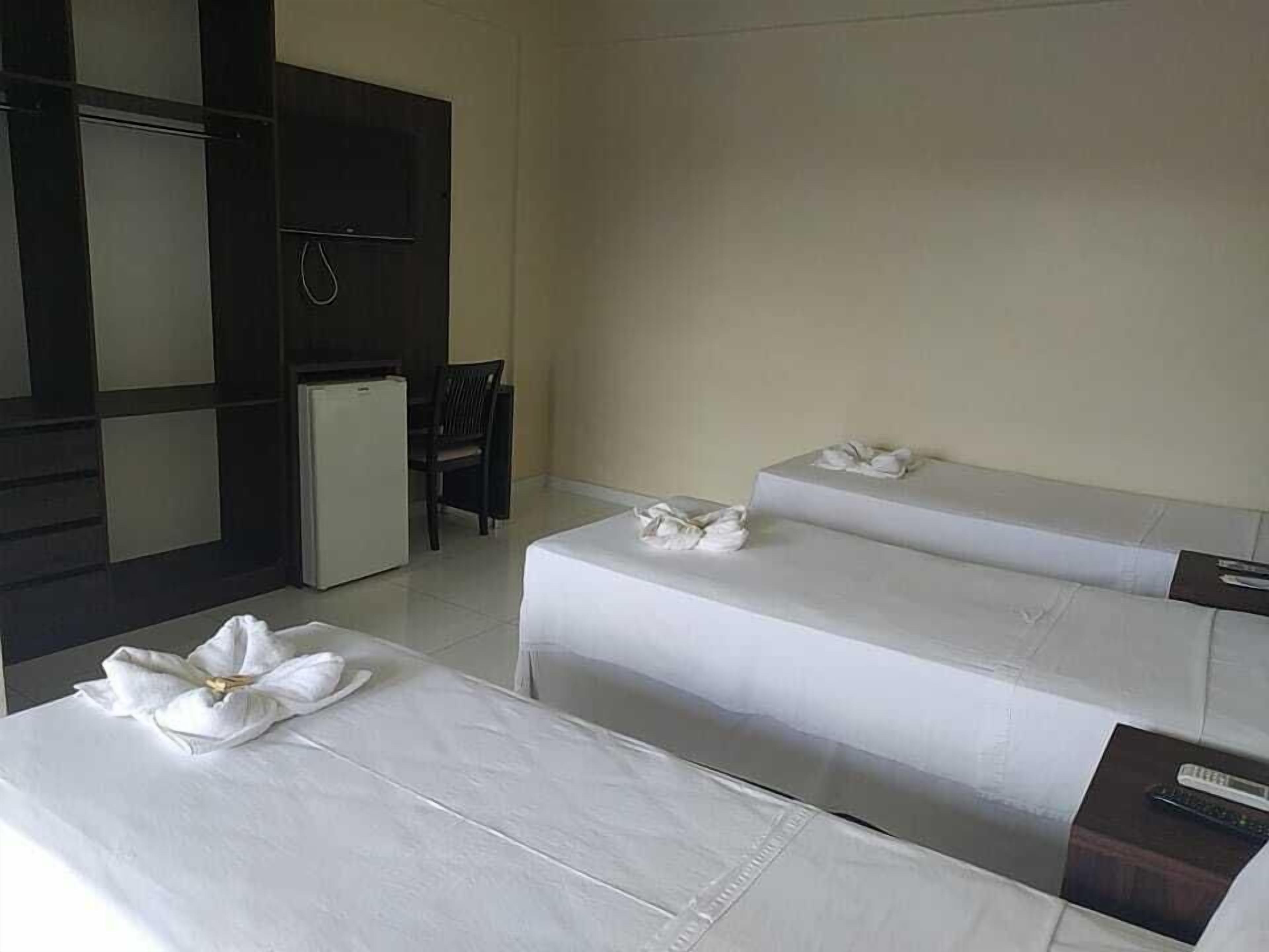 Habitación de hotel con dos camas, un escritorio pequeño, una silla, televisor y refrigerador.