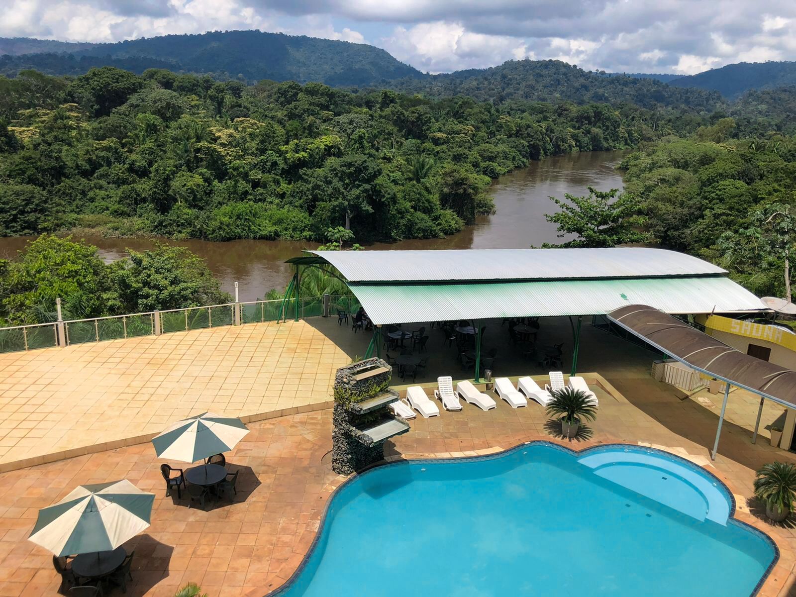 A pool area with lounge chairs and umbrellas, overlooking a river and forested hills.